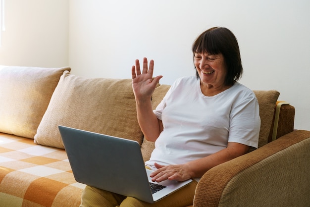 Oudere volwassen vrouw die draadloze laptop-apps gebruikt die op internet surfen, zittend op de bank glimlachend van middelbare leeftijd