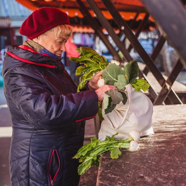 Oudere vrouw die een eco-boodschappentas vasthoudt terwijl ze op een voedselmarkt staat