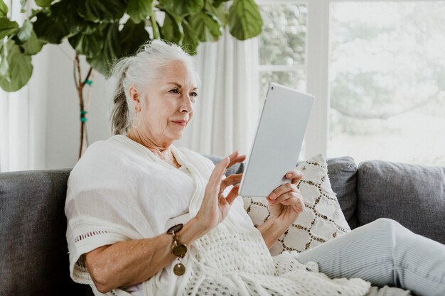 Oudere vrouw die een tablet op een bank gebruikt