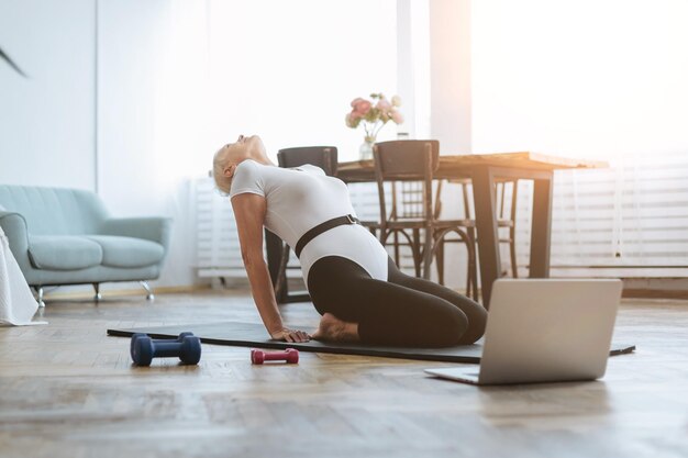 Oudere vrouw die fitness doet met een online trainer in haar woonkamerconcept van een gezonde levensstijl