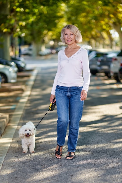 Oudere vrouw die met een hond buiten loopt.