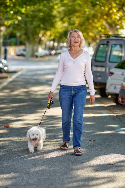 Oudere vrouw die met een hond buiten loopt.