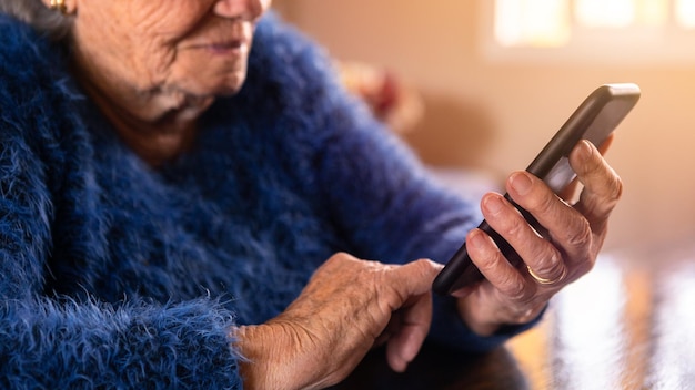 Oudere vrouw die mobiele telefoon gebruikt terwijl ze in de woonkamer thuis zit Grootmoeder