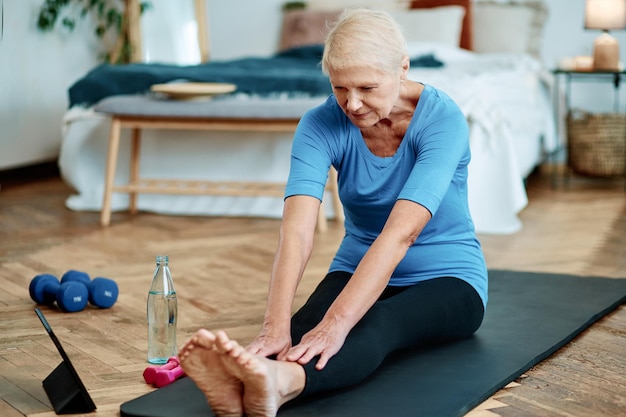Oudere vrouw die pilates gymnastiek online uitvoert in haar woonkamerconcept van een gezonde levensstijl