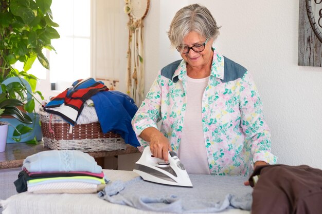 Oudere vrouw die thuis kleren strijkt