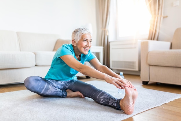 oudere vrouw die thuis opwarmt Fitness vrouw die stretch oefeningen doet haar benen strekt squadriceps Oudere vrouw die een actieve levensstijl heeft