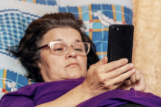Oudere vrouw die tijdens ziekte in bed ligt met een telefoon in haar handen