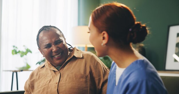 Oudere vrouw en verzorger met praten of lachen op de bank in een verpleeghuis voor steun grappig verhaal en vriendelijkheid Oudere persoon verpleegster en gelukkig in hospice met mededogen begrip en grap