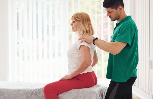 Oudere vrouw heeft een bezoek aan de kliniek en is aan het revalideren Mannelijke instructeur helpt haar