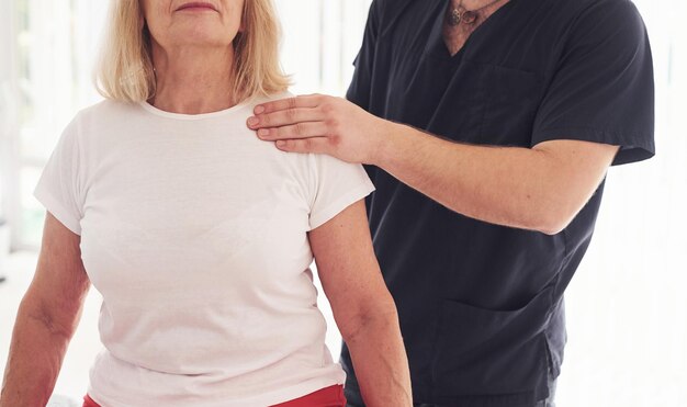 Foto oudere vrouw heeft een bezoek aan de kliniek en is aan het revalideren mannelijke instructeur helpt haar