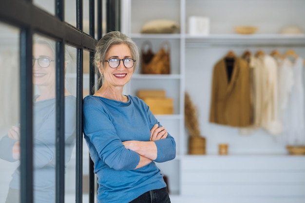 Oudere vrouw houdt de armen gevouwen op haar borst en kijkt met een zelfverzekerde glimlach naar de camera