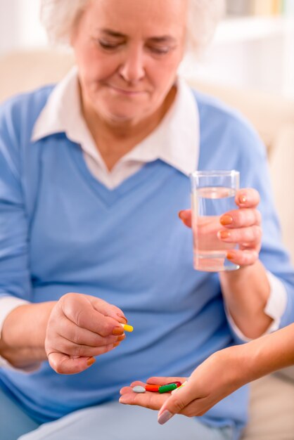 Oudere vrouw houdt een glas water en neemt een pil.