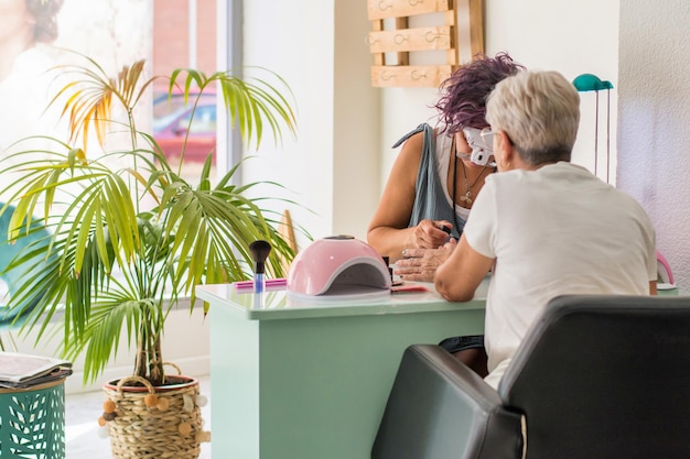 Oudere vrouw krijgt een manicure in een schoonheidssalon. Schoonheidsspecialiste werkt in haar werkruimte. Klein bedrijf