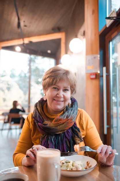 Oudere vrouw luncht in café met Caesarsalade en koffie