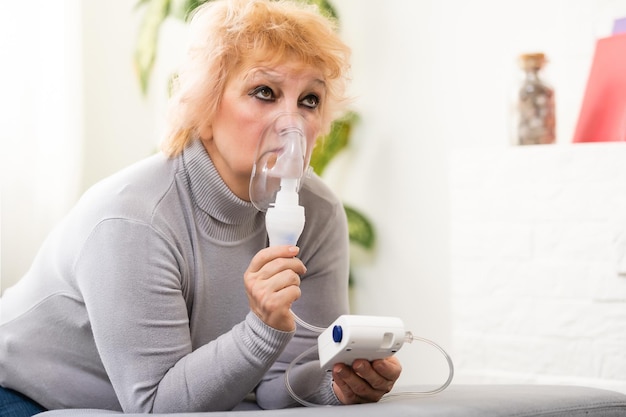 Oudere vrouw met astma machine op lichte achtergrond.