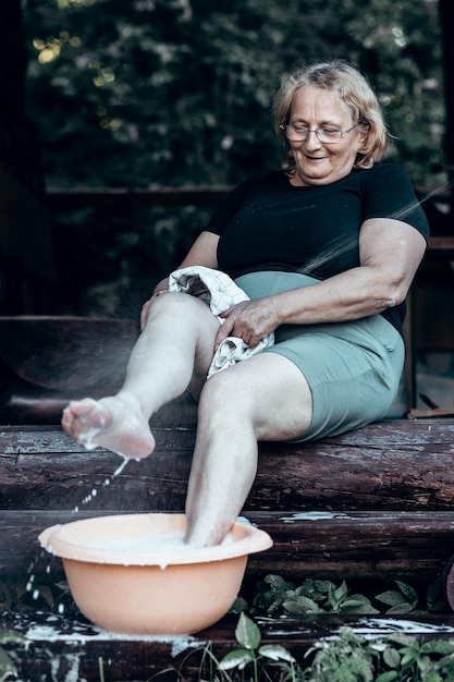 Oudere vrouw met een bril die haar voeten in de wasbak wast