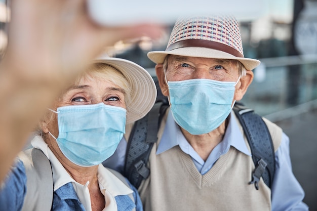 Oudere vrouw met een gezichtsmasker die zichzelf en haar echtgenoot fotografeert met de mobiele telefoon