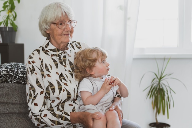 Oudere vrouw met haar kleine kleinzoon die thuis op de bank speelt