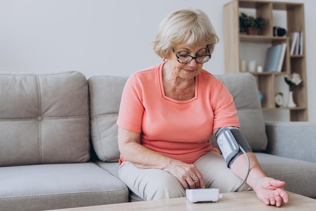 Oudere vrouw met hypertensie die zelf thuis haar bloeddruk meet Droevige volwassen dame die haar bloeddruck meet met behulp van een tonometer Dagelijkse gezondheidscontrole