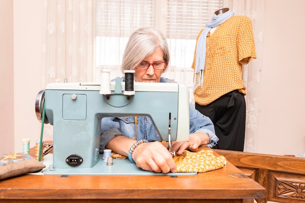 Oudere vrouw naait een oranje doek met een antieke naaimachine