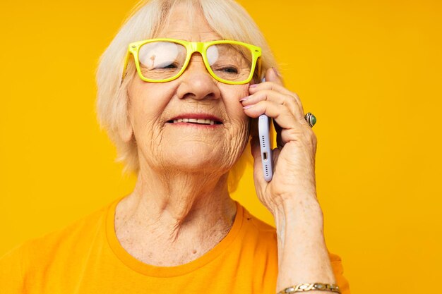 Oudere vrouw praten aan de telefoon in gele glazen geïsoleerde achtergrond