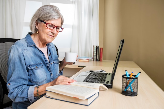 Oudere vrouw studeert met een laptop en boeken op een bureau