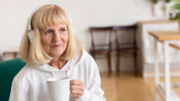 Oudere vrouw thuis genieten van koffie en muziek op de koptelefoon