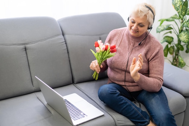 Oudere vrouw videobellen op laptop, zwaaien naar scherm, chatten met kinderen, vrije ruimte.