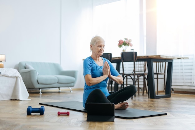 Oudere vrouw zit in een yoga-pose voor een opengeklapte laptop