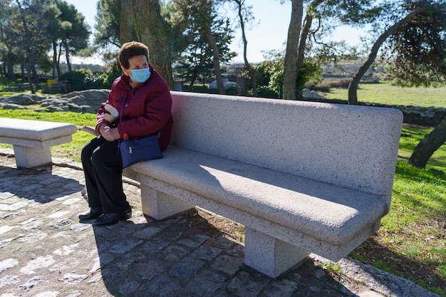 Oudere vrouw zittend op een bankje met sociale afstand nemen vanwege coronavirus.