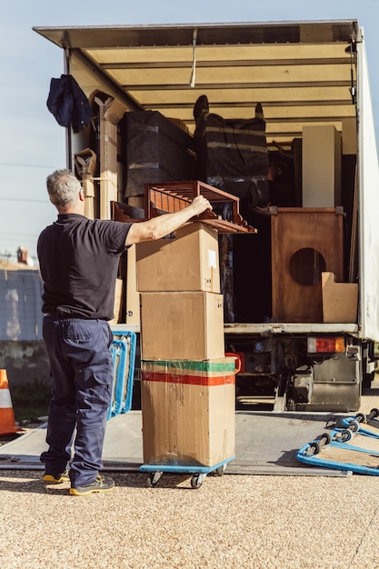 Foto oudere werknemer brengt een stapel kartonnen dozen naar een vrachtwagen in een rijdende operatie