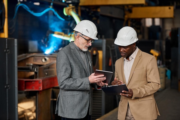 Oudere zakenman die de resultaten op tablet-pc aan zijn collega laat zien terwijl hij het formulier indient tijdens hun werk in de fabriek