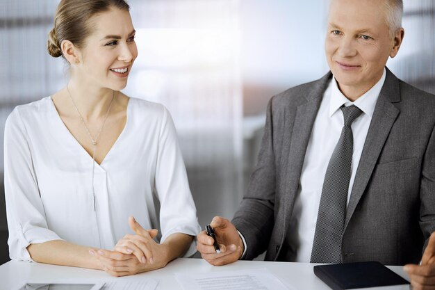 Oudere zakenman en vrouw zitten en communiceren in zonnig kantoor. Volwassen zakenmensen of advocaten werken samen als partners en collega's tijdens een vergadering.