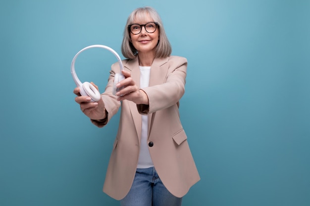 Oudere zakenvrouw die naar muziek luistert in een grote koptelefoon op een lichte achtergrond met kopieerruimte