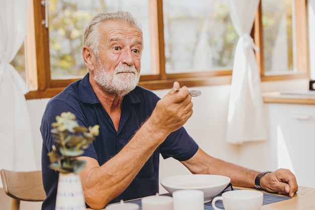 Ouderling die gezichtsuitdrukking eet, voelt verrassing met een zeer goede smaak van eten door zijn vrouw