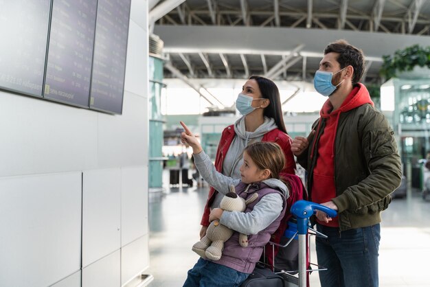 Ouders die beschermende maskers dragen die voor het tijdschemabord op de luchthaven staan