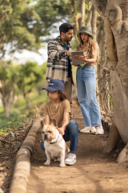 Ouders die een digitale tablet checken tijdens een excursie met hun zoon en een hond