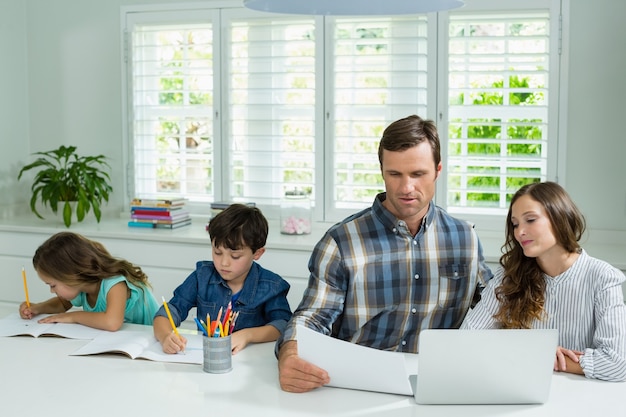 Ouders die met laptop werken en kinderen studeren in de woonkamer