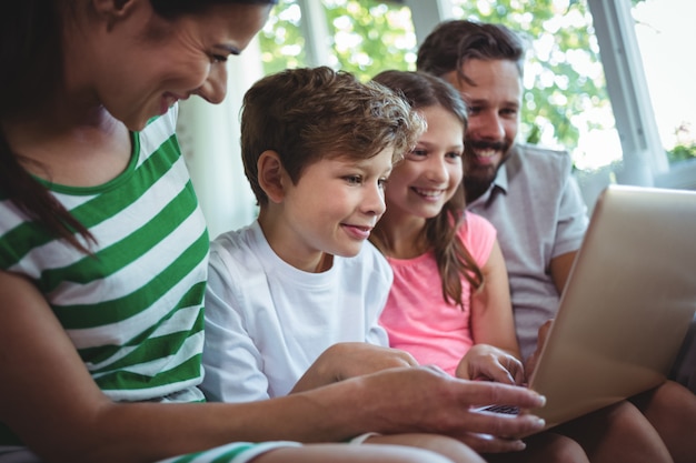 Ouders die op bank met hun kinderen zitten en laptop in woonkamer met behulp van