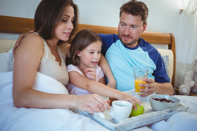 Ouders die op bed met dochter zitten en ontbijt hebben