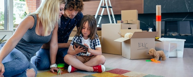 Foto ouders die toezicht houden op hun zoontje terwijl hij de tablet speelt terwijl hij op de vloer van de woonkamer zit