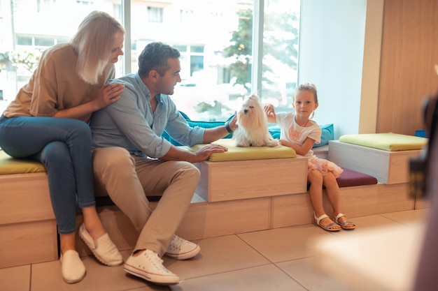 Ouders en dochter aaien hun schattige pluizige witte hond