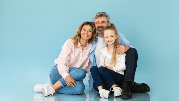 Ouders en dochtertje zitten en knuffelen op blauwe achtergrond