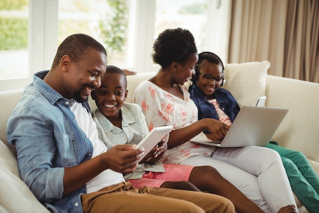 Ouders en kinderen met behulp van laptop en digitale tablet op sofa