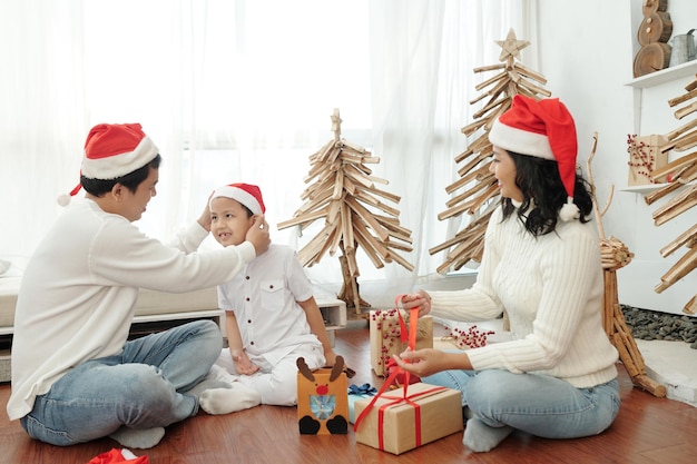 Ouders en zoon in santa claus hoeden maken zich klaar voor kerstviering thuis