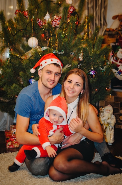 Ouders houden kleine jongen zit in de buurt van de kerstboom.