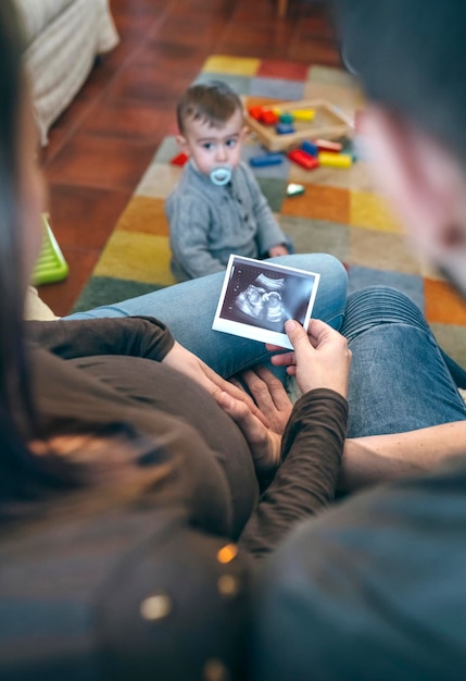 Ouders kijken naar de echo van hun nieuwe baby terwijl de oudere broer speelt