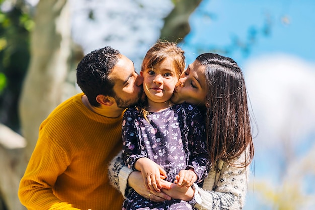 Ouders kussen schattige dochter terwijl ze tegen de hemel staan in het park
