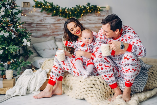 Ouders met hun dochtertje in vakantiekleding met bedrukte herten en sneeuwvlokken zittend op het bed met kopjes thee in een gezellige kamer