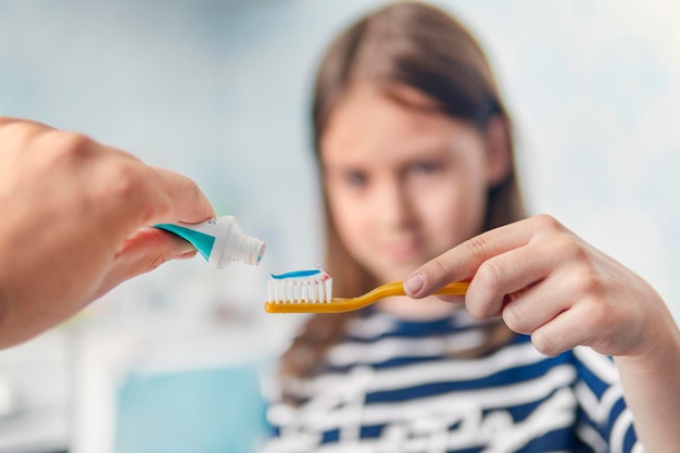 Ouders voor mondhygiëne, de vader drukt een kleurrijke tandpasta op de tandenborstel in het kind